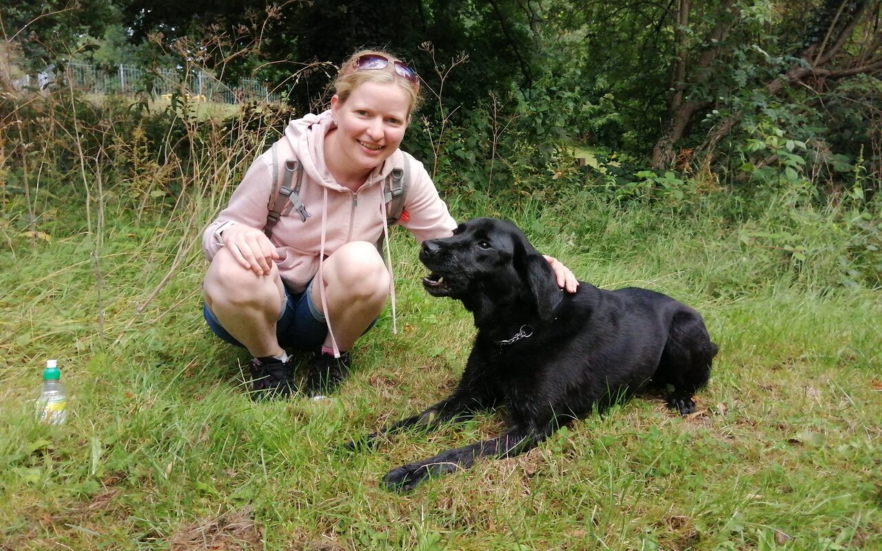 Tal's Pals owner Chantal crouching in a field beside a black labrador.